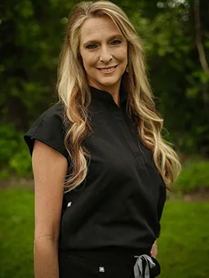 A smiling woman with wavy hair in black scrubs.